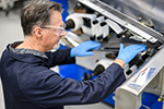 Person wearing safety glasses and blue gloves operating industrial manufacturing equipment.