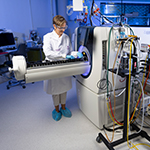 Laboratory technician holding a cylindrical component beside specialized testing equipment in a research laboratory