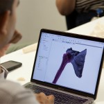 Person looking at laptop screen with 3D printed human shoulder components