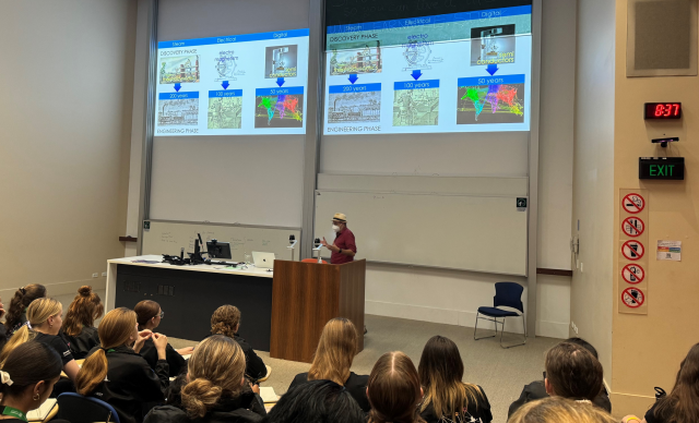 Professor Andrew White standing at a podium front of a class with a large screen on the wall