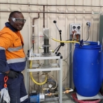 Worker standing beside industrial water treatment equipment with a blue drum and connected piping.