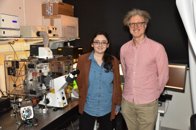 PhD student Larnii Booth and Prof Warwick Bowen standing in front of a microscope, engaged in scientific observation.