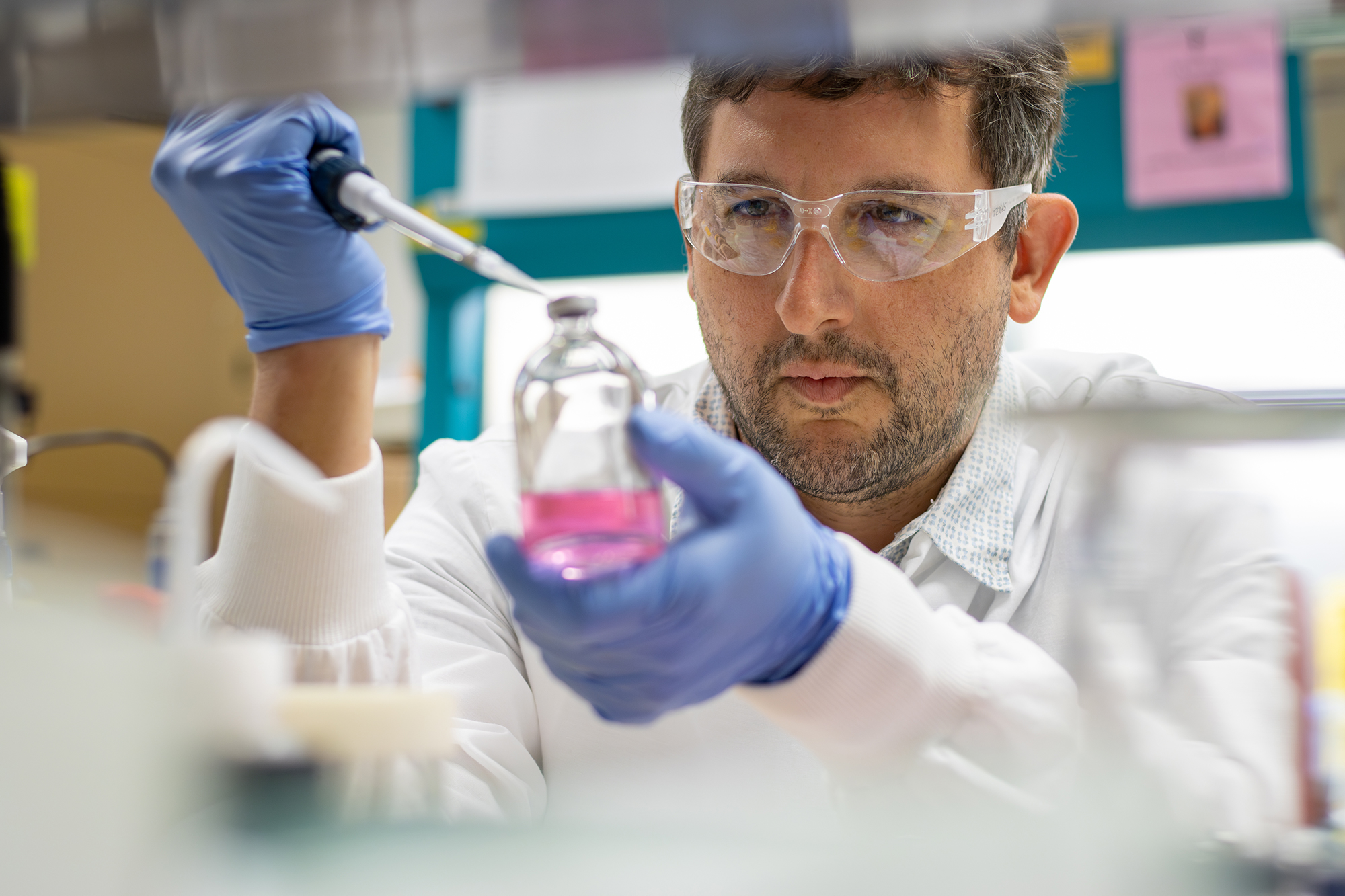 Scientist pipetting into a glass bottle wearing protective gloves and glasses.